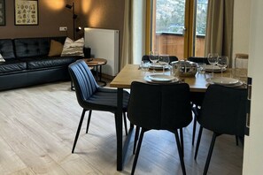 Ein Essbereich mit einem Holztisch, gedeckt für vier Personen, schwarzen Stühlen und einer schwarzen Ledersofa im Hintergrund.