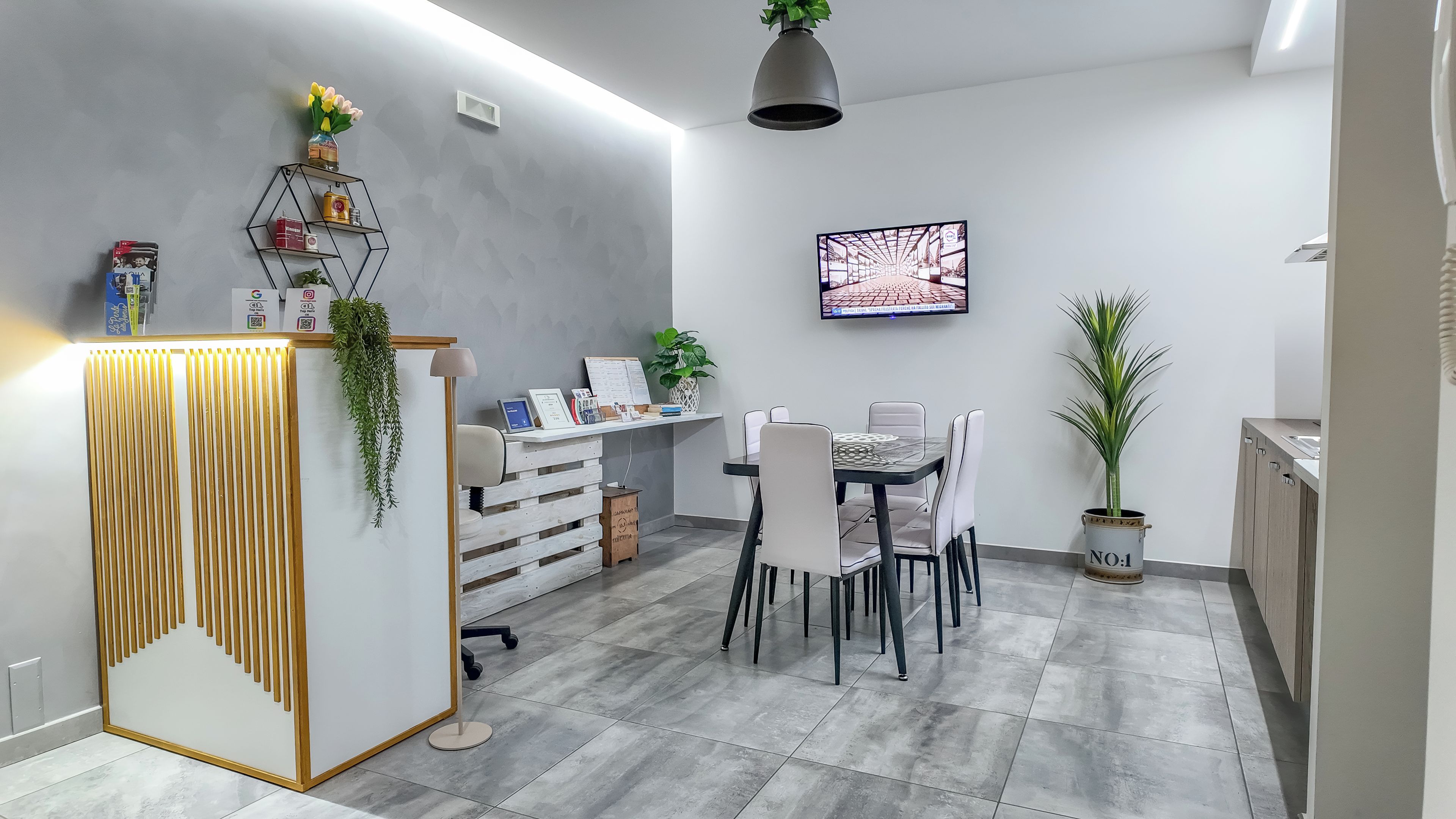 Zona pranzo moderna con tavolo e sedie, una TV a muro e una pianta in vaso.