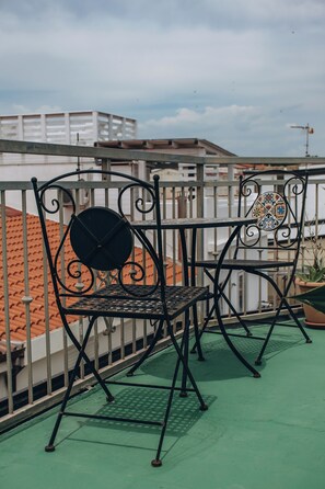 A metal balcony with two chairs and a table, overlooking a building with red-tiled roofs. - Four Winds B&B: 50 meters from the beach and the Aragonese Castle; Wi-Fi and AC (Le Castella)