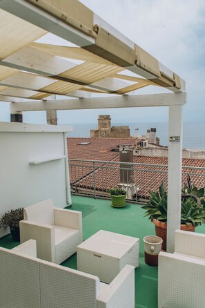 Terrassa al terrat amb mobiliari exterior, una pèrgola i vistes al mar i edificis històrics.