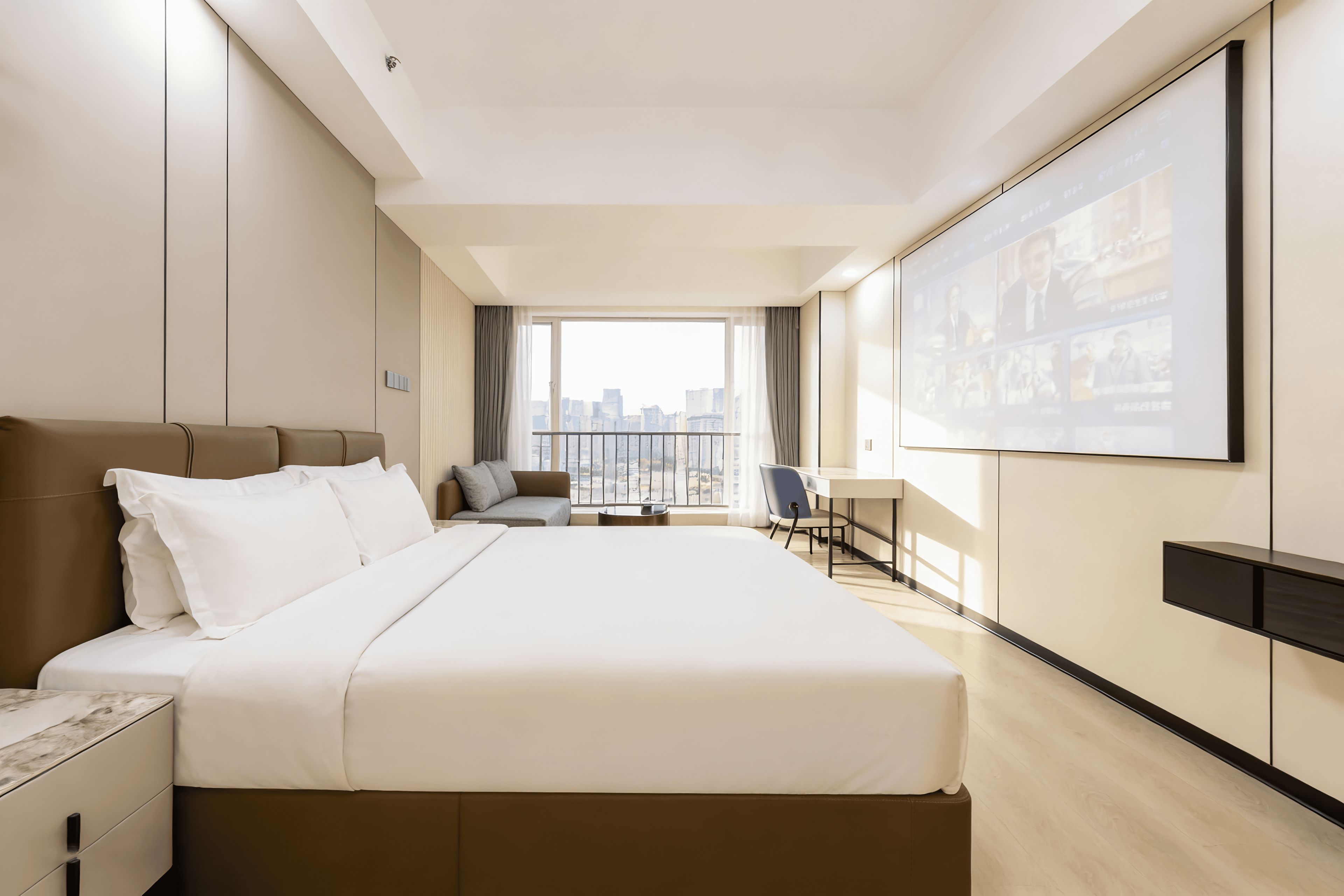 A hotel room with a large bed, a desk, a chair, and a view of the city through the window.