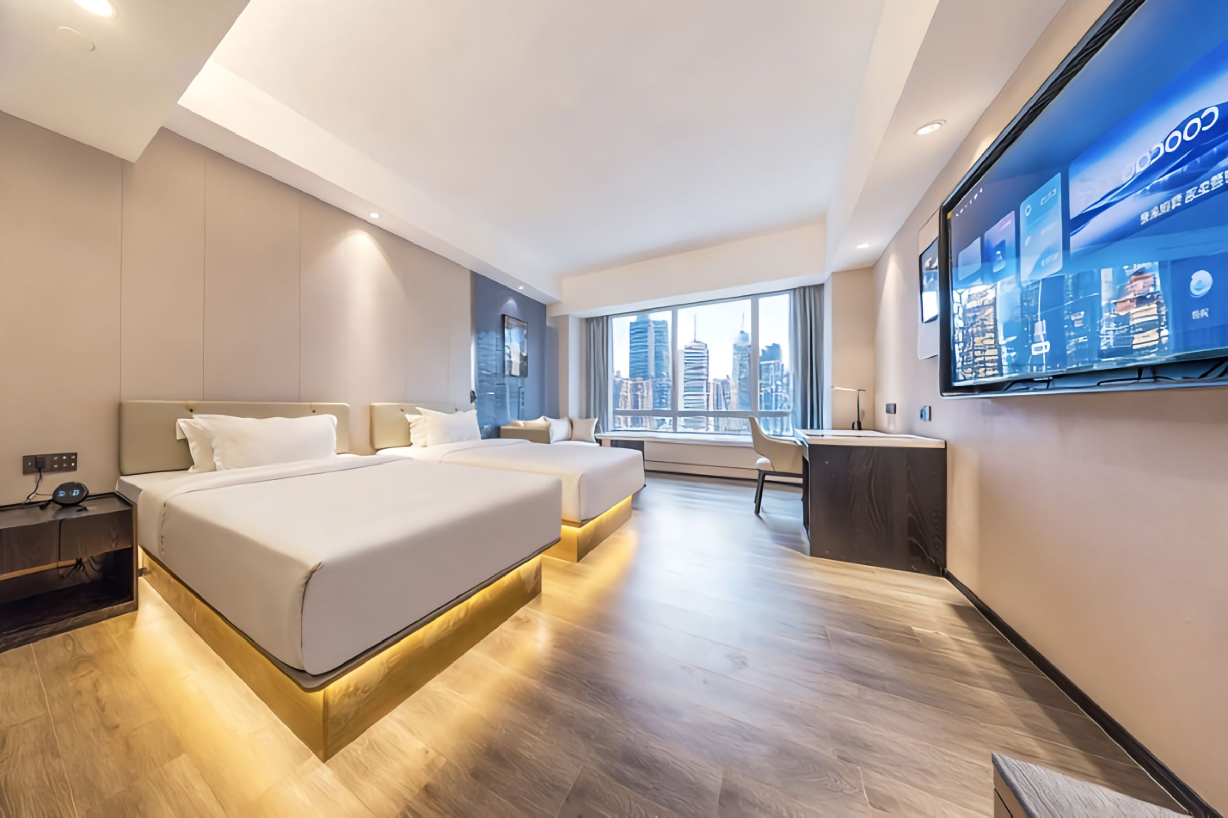 Une chambre d’hôtel moderne équipée de deux lits, d’un bureau, d’une grande fenêtre donnant sur la ville et d’un téléviseur à écran plat fixé au mur.