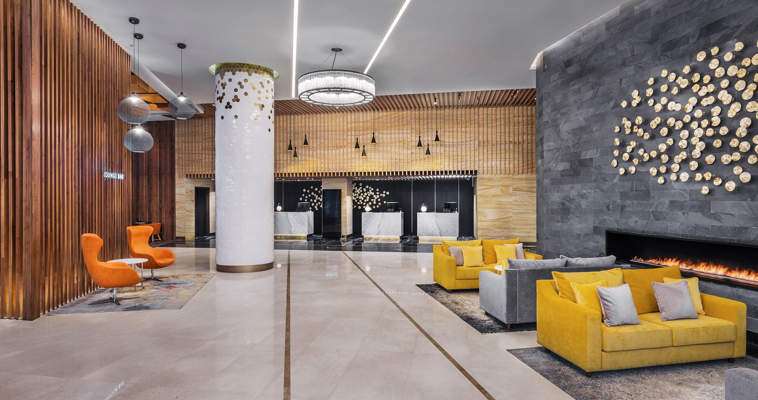 A modern lobby with a central column, seating areas, a fireplace, and a reception desk.
