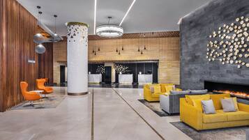 A modern lobby with a central column, seating areas, a fireplace, and a reception desk.