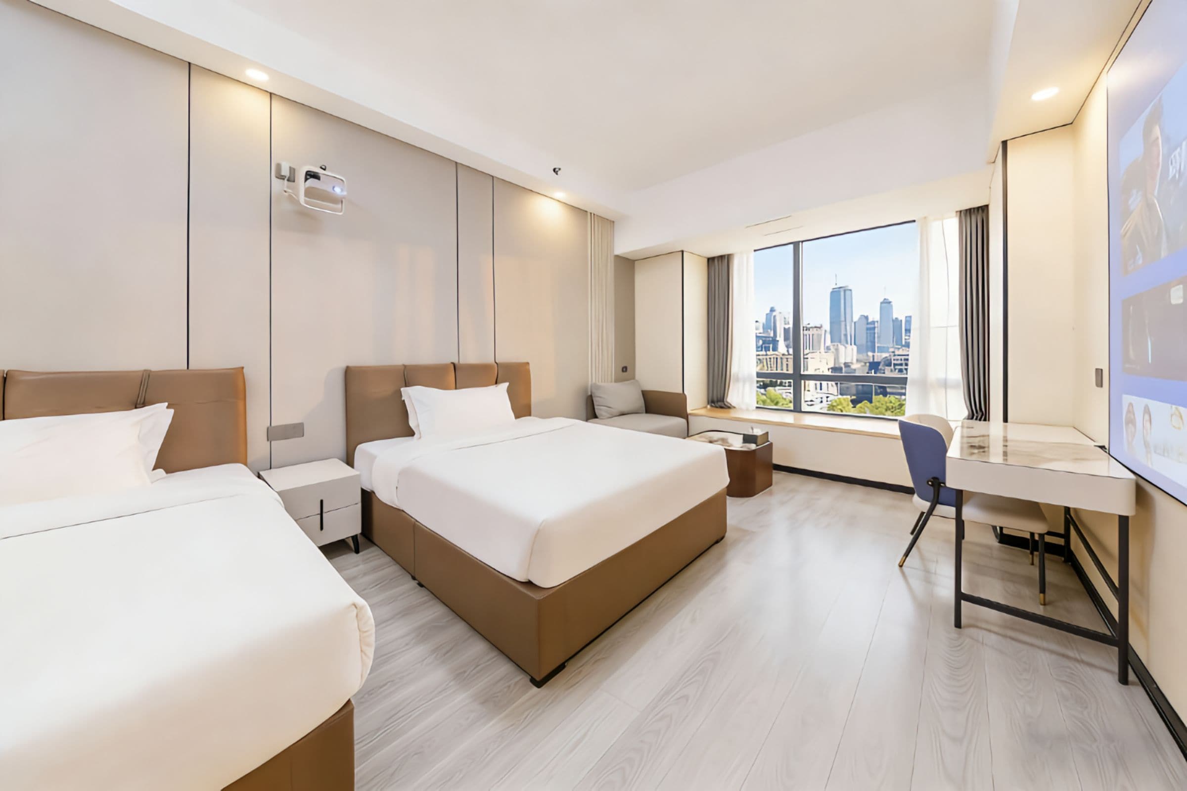 Een hotelkamer met twee bedden, een bureau en een groot raam met uitzicht over de stad.