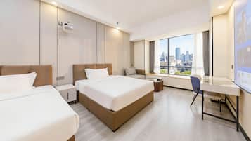 Een hotelkamer met twee bedden, een bureau en een groot raam met uitzicht over de stad.
