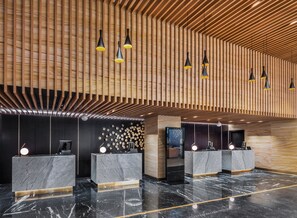 Una moderna zona de recepción con mostradores de mármol, techo de listones de madera e iluminación colgante.