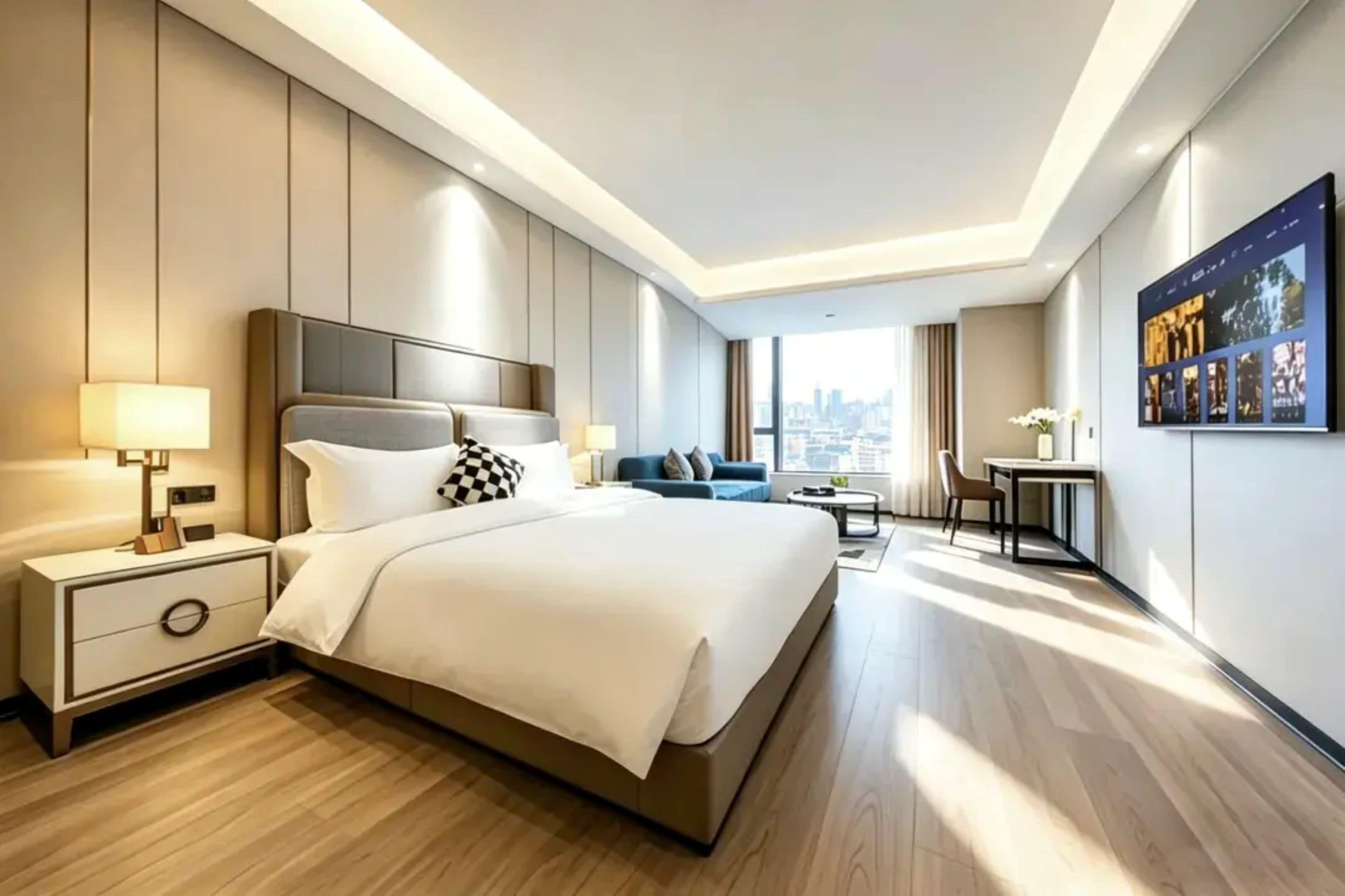A modern hotel room with a large bed, bedside tables, a desk, and a city view.
