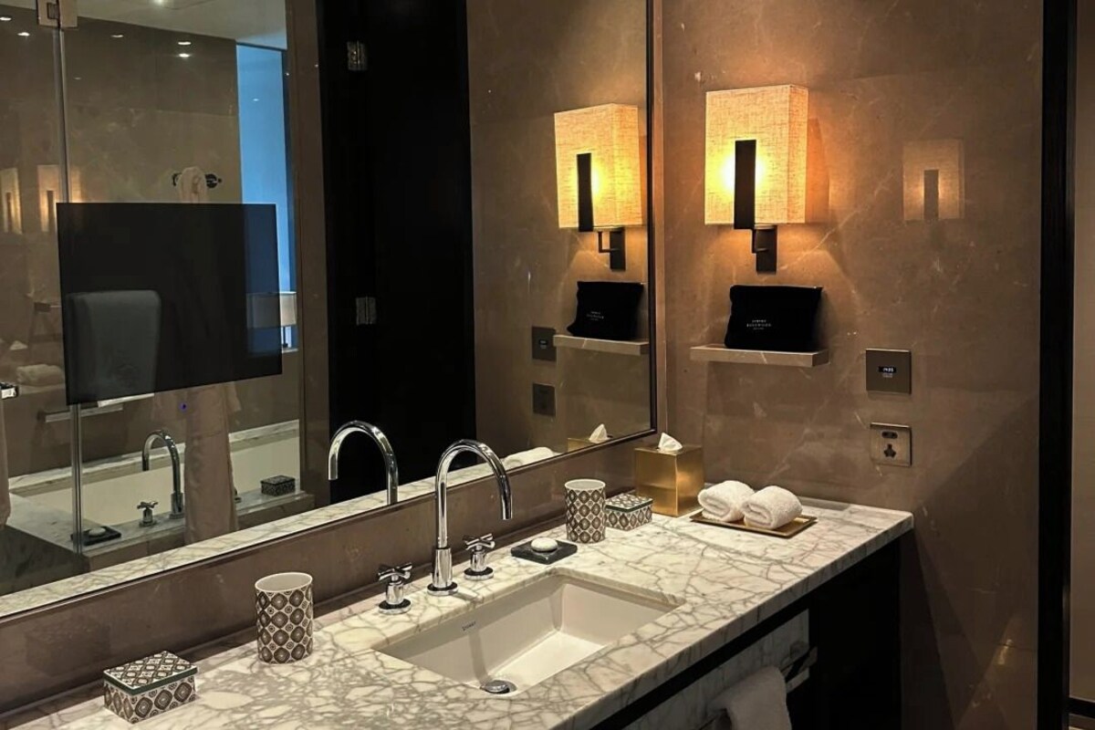 A modern bathroom with a large mirror, two wall-mounted lights, a marble sink, and a towel rack.