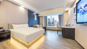 A modern hotel room with a large bed, a desk, and a city view.