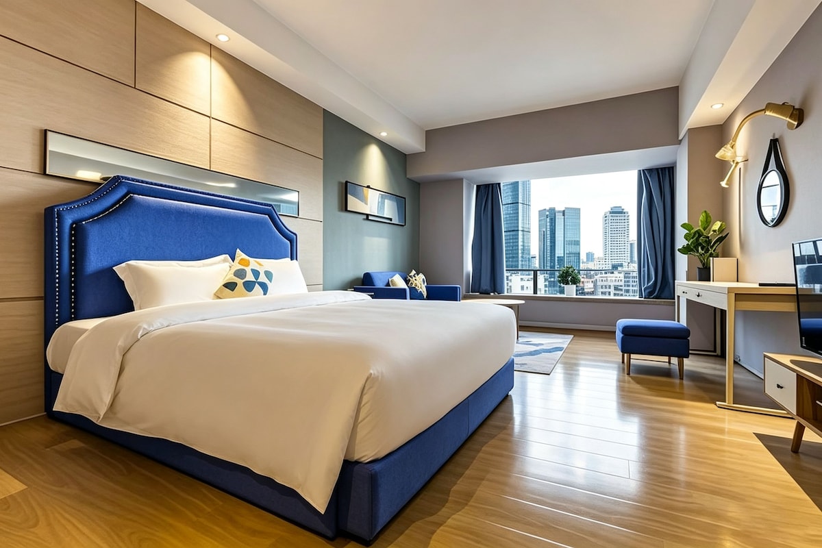 A modern hotel room with a large bed, a desk, and a view of the cityscape.
