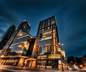 Um edifício moderno de grande porte com fachada de vidro refletivo e uma entrada destacada com marquise.