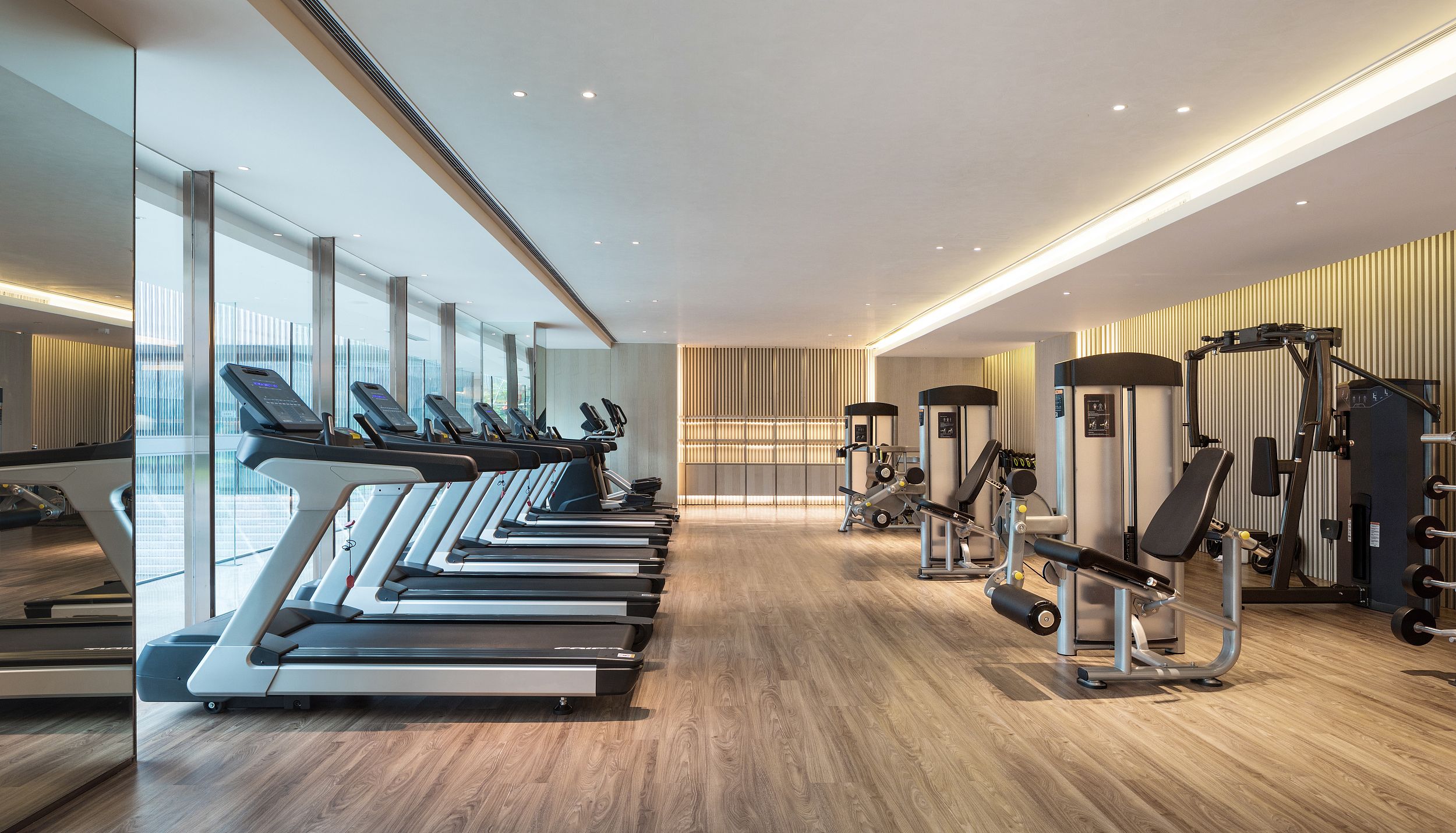 A modern gym with treadmills, weight machines, and a wooden floor.