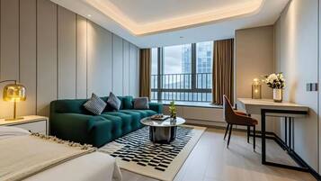 A modern hotel room with a green sofa, a small round coffee table, a desk with a chair, and a large window with curtains.
