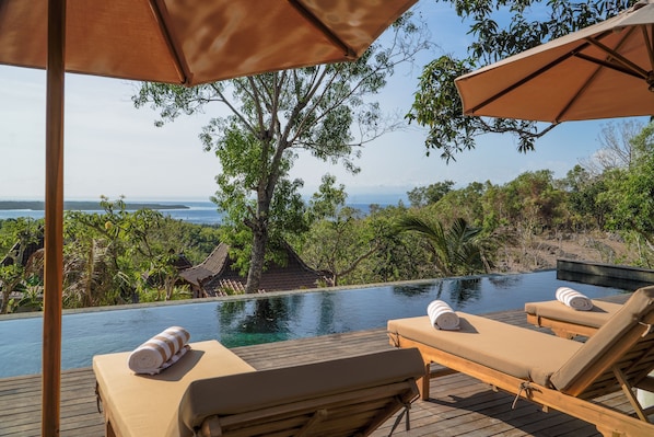 An infinity pool with lounge chairs and umbrellas, overlooking a natural landscape and the sea. - La Colline Nusa Penida (Penida Island)