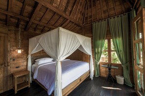 A wooden cabin room with a four-poster bed, a small table, and a window with curtains. - La Colline Nusa Penida (Penida Island)