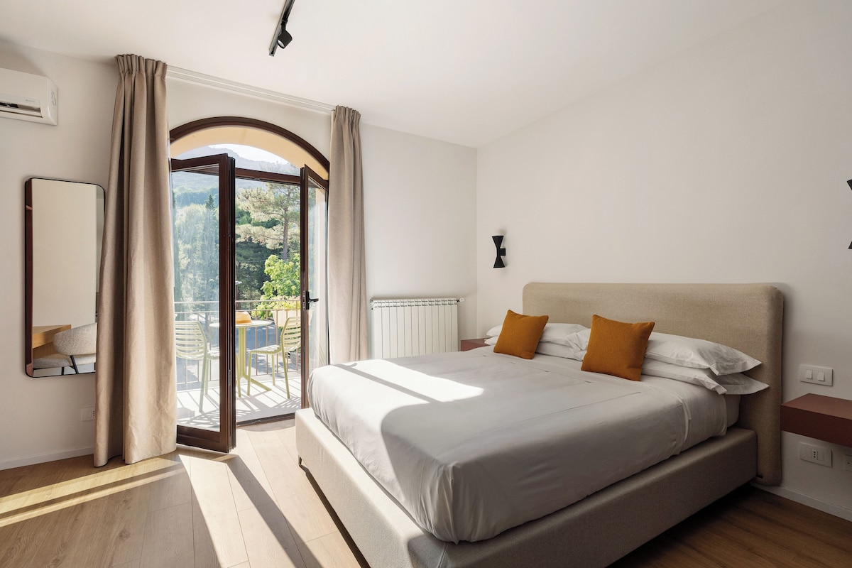 Un dormitorio con una cama grande, vistas a un espacio exterior por una puerta abierta, un radiador y un aplique de pared.