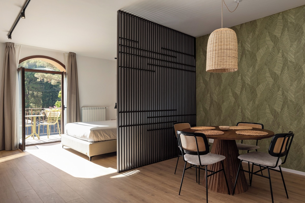 Un dormitorio moderno con una cama, una zona de comedor con mesa y sillas, y vistas al exterior mediante una puerta corredera.