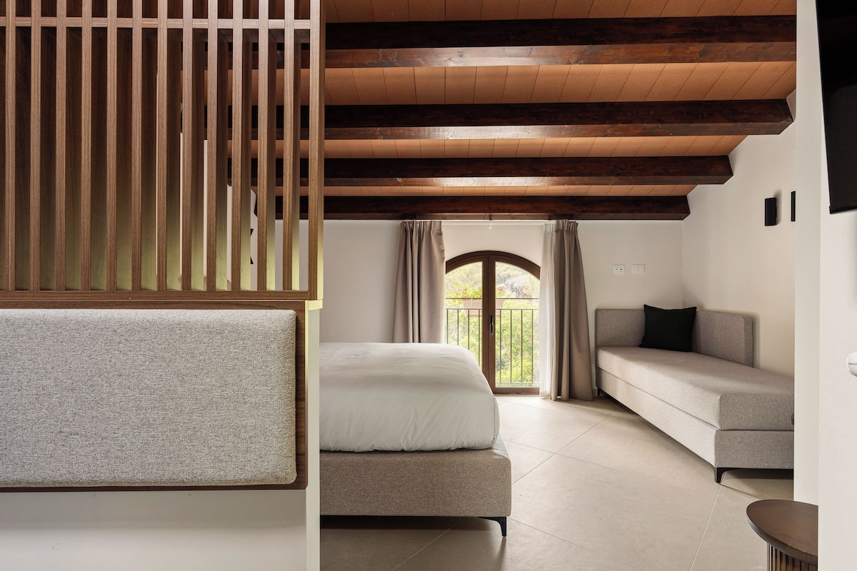 Un dormitorio con cama, sofá, techo de madera y ventana con cortinas.