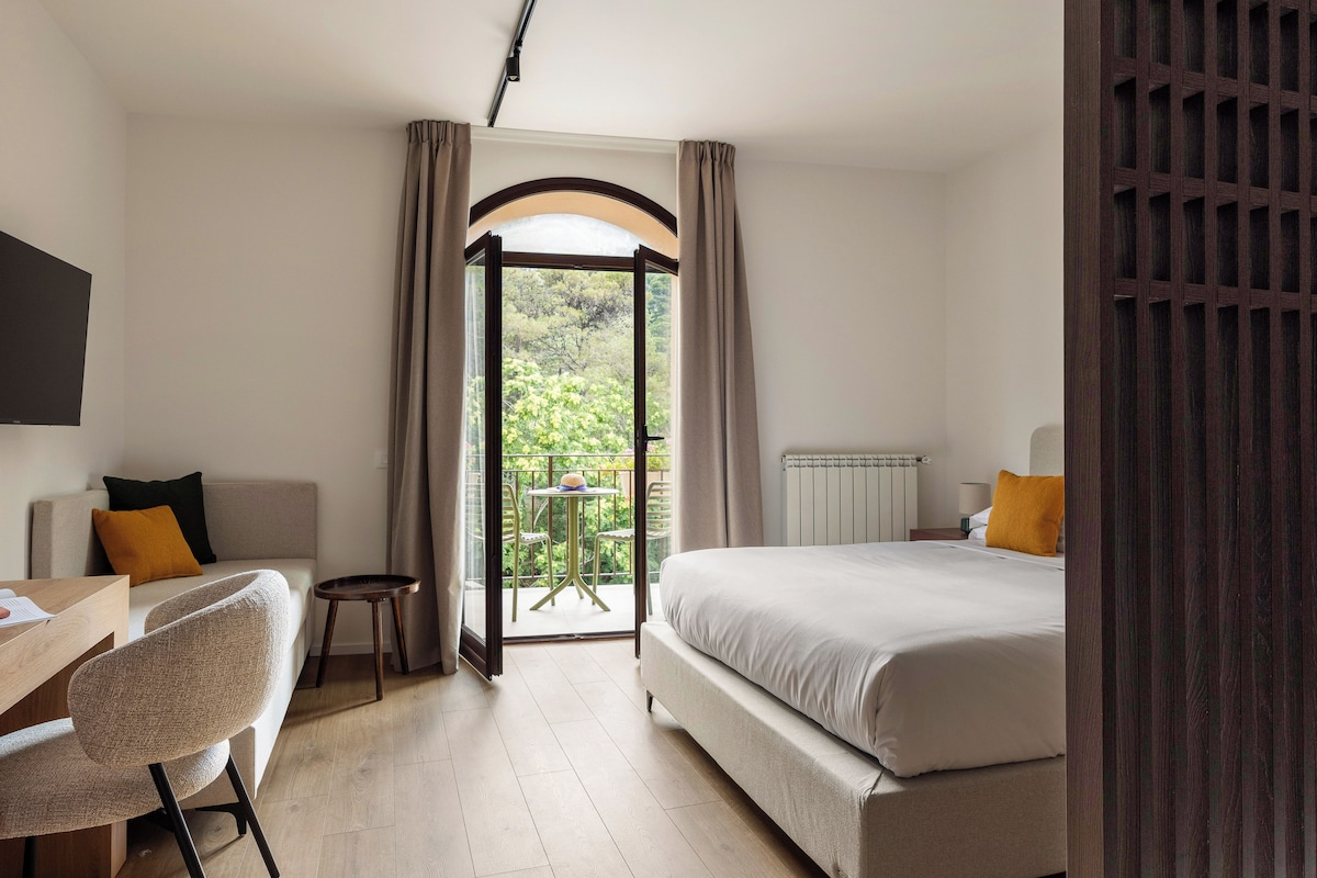 Habitación de hotel con cama, escritorio, silla y vista al exterior a través de una puerta de vidrio.