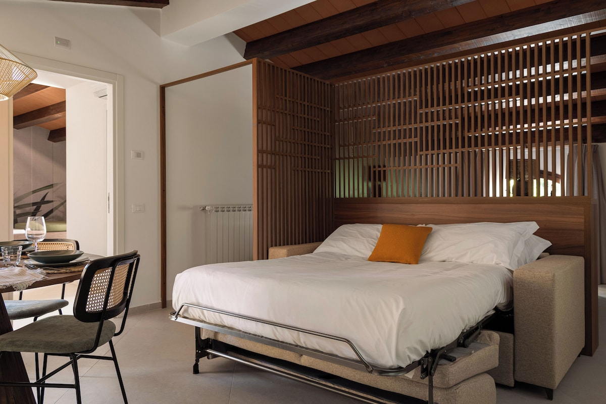 Una cama con cabecera, una mesa de comedor con sillas y una ventana con persianas.