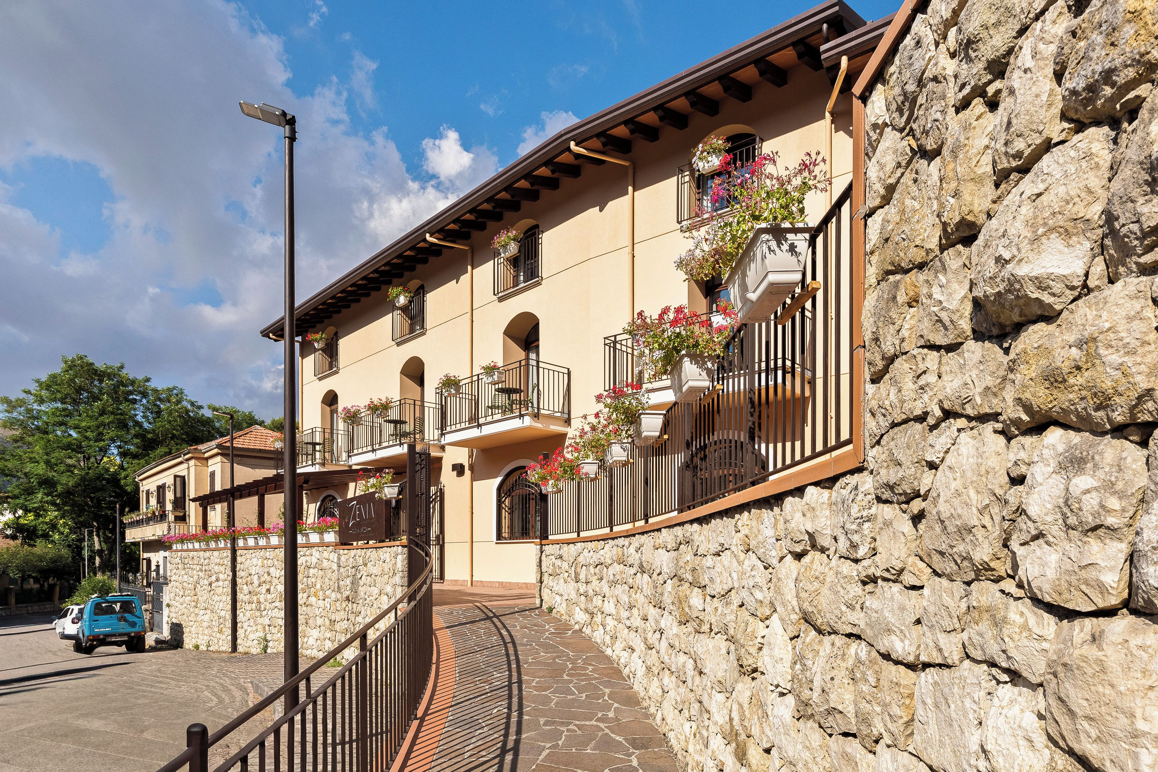 Un edificio de varios pisos con muros de piedra, balcones con jardineras y un cielo despejado.