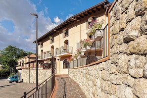 Un edificio de varios pisos con muros de piedra, balcones con jardineras y un cielo despejado.