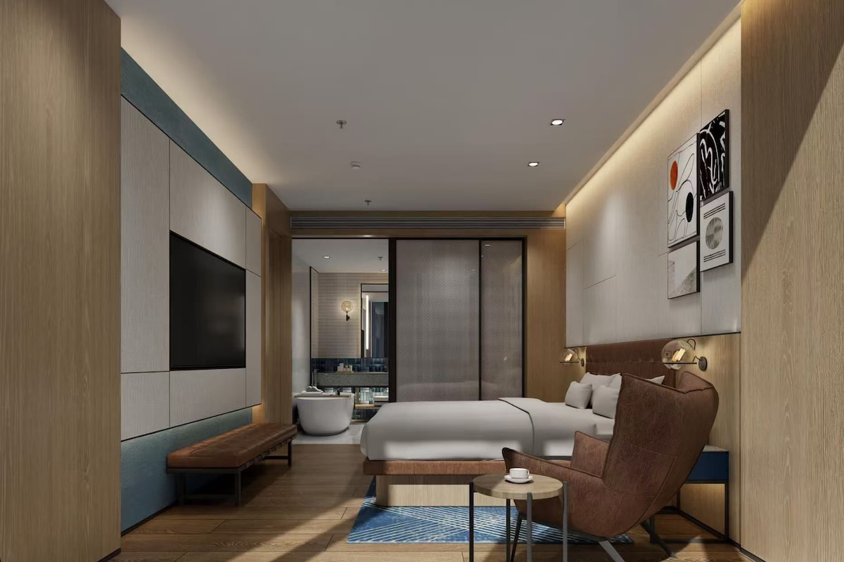 A modern hotel room with a bed, seating area, and a TV.