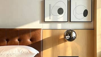 A hotel room with a bed, a bedside table, a mirror, and abstract artwork on the wall.