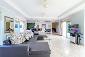 A modern living room with a sofa, a television, and a kitchen in the background. - Spacious 5BR Villa with Pool&Annex (JB1) (Pattaya)