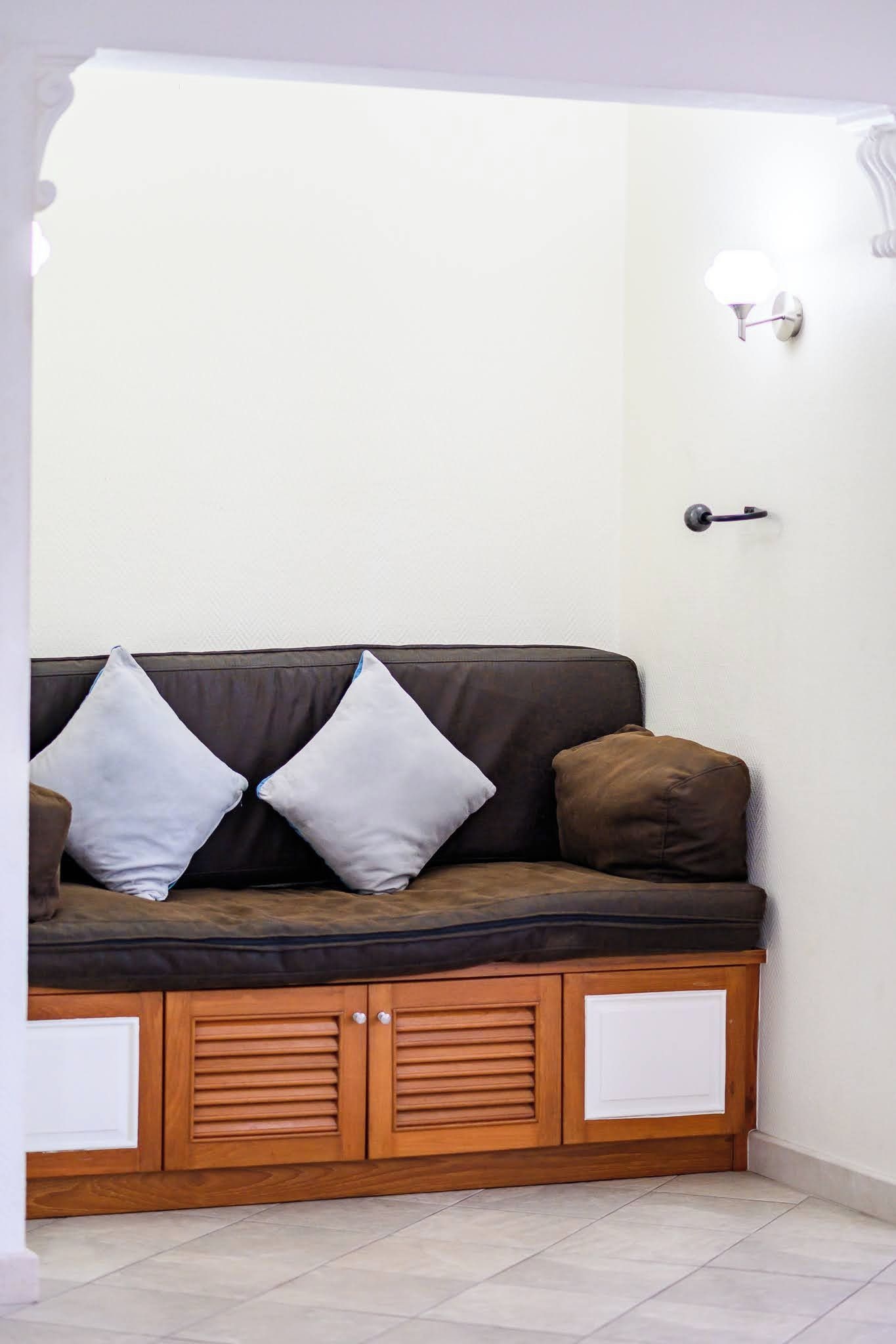Une pièce d’angle avec un canapé marron, deux coussins blancs, un meuble en bois et une porte avec une clé.