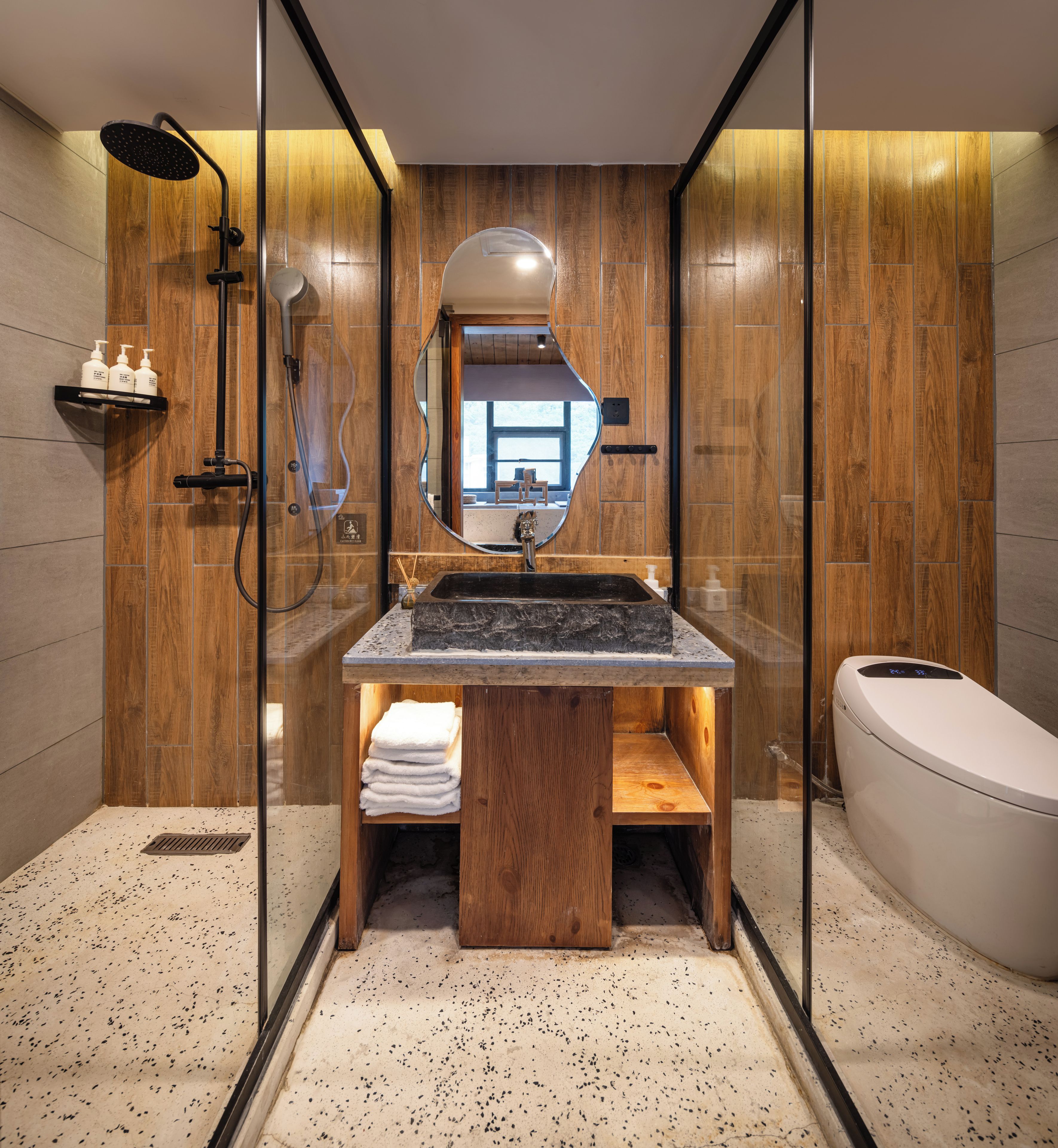 A modern bathroom with a wooden vanity, a glass shower enclosure, and a white toilet.