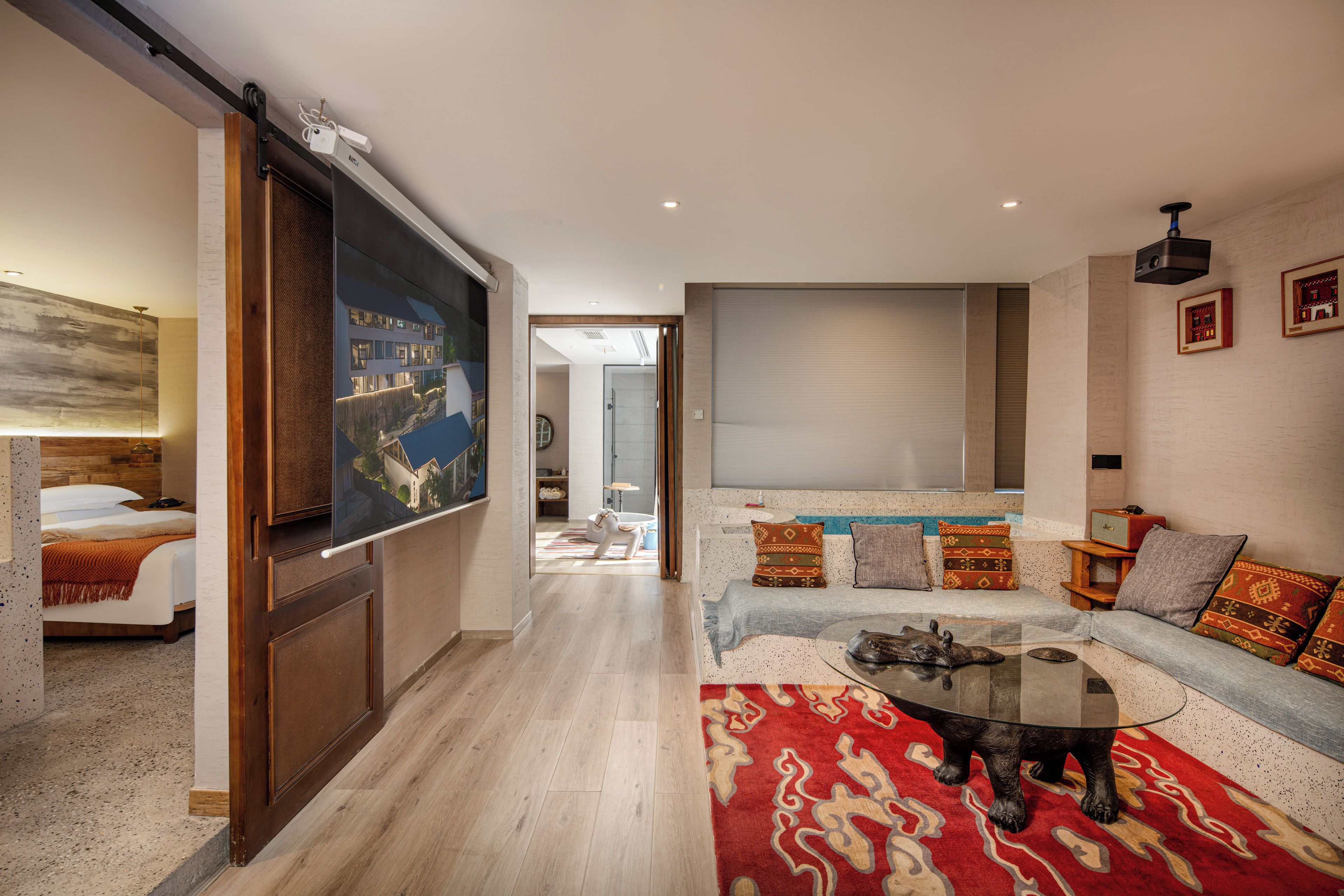 A modern living room with a large flat-screen TV, a sofa with patterned cushions, a coffee table, and a wooden floor.