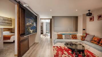 A modern living room with a large flat-screen TV, a sofa with patterned cushions, a coffee table, and a wooden floor.