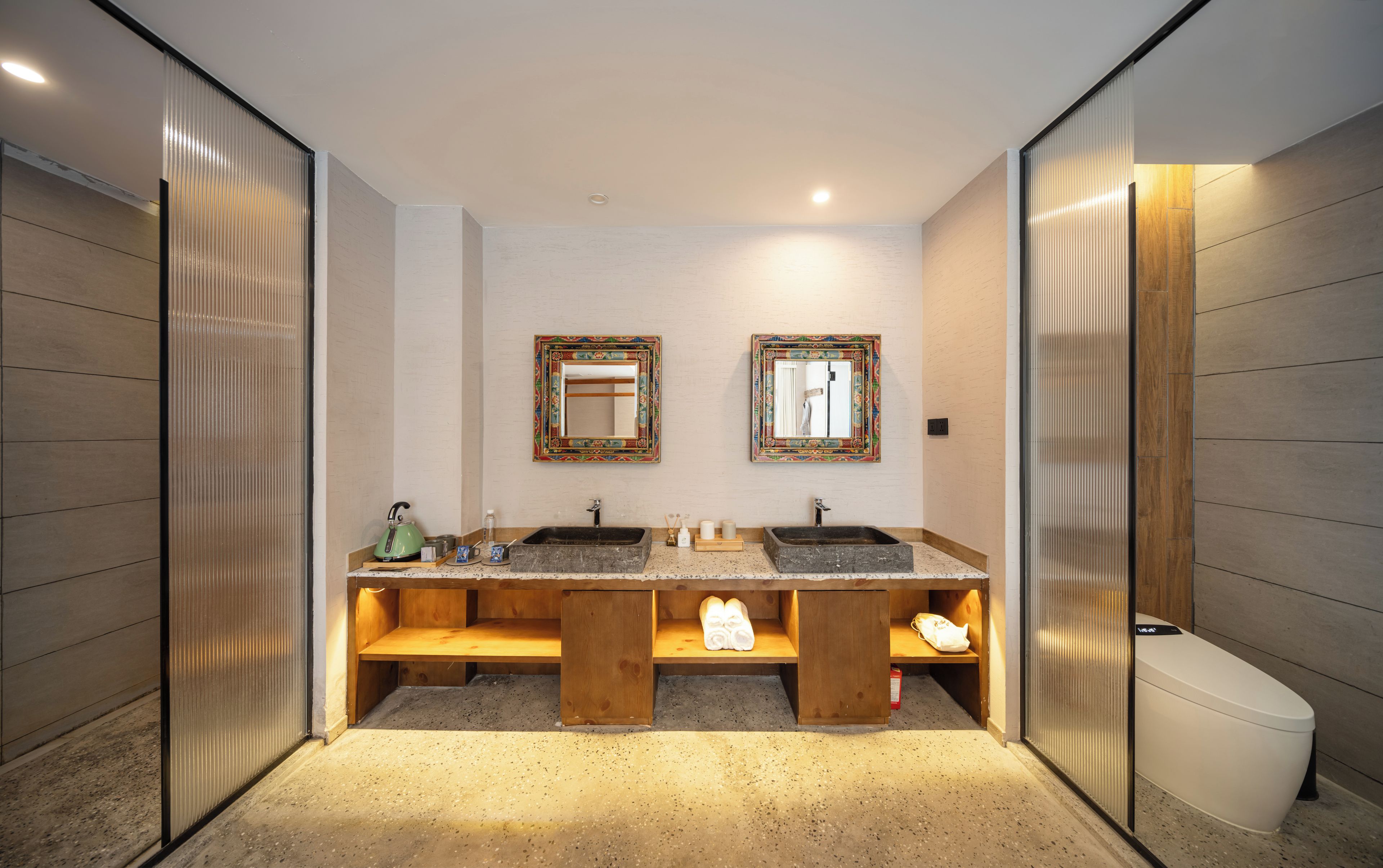 A modern bathroom with two sinks, wooden benches, and a toilet.