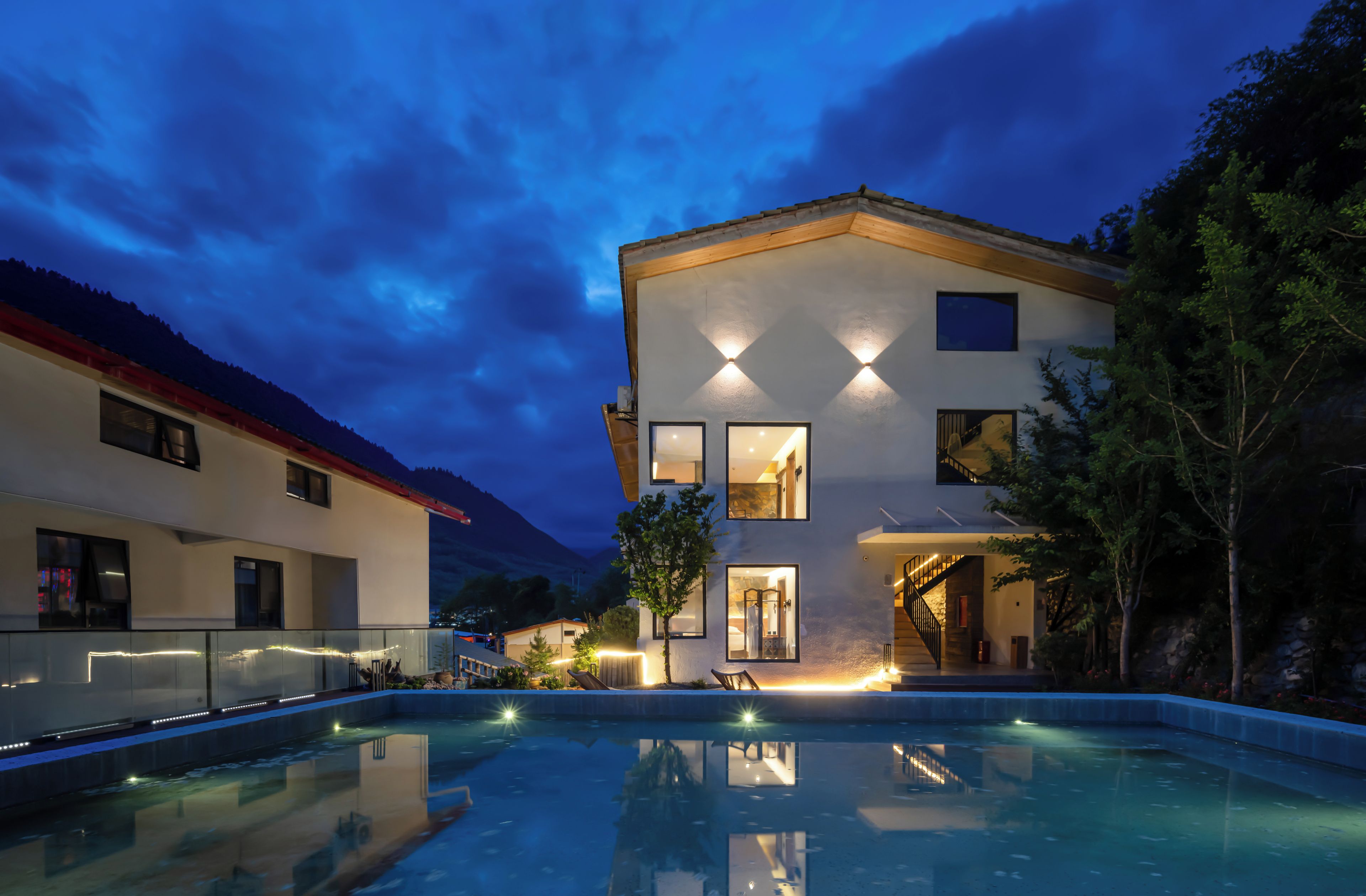 Uma casa moderna de dois andares com piscina, grandes janelas e vista para as montanhas.