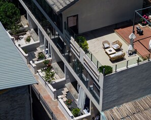 Un edificio moderno con terraza en la azotea, mobiliario exterior, un pequeño jardín y una estatua decorativa de un oso.