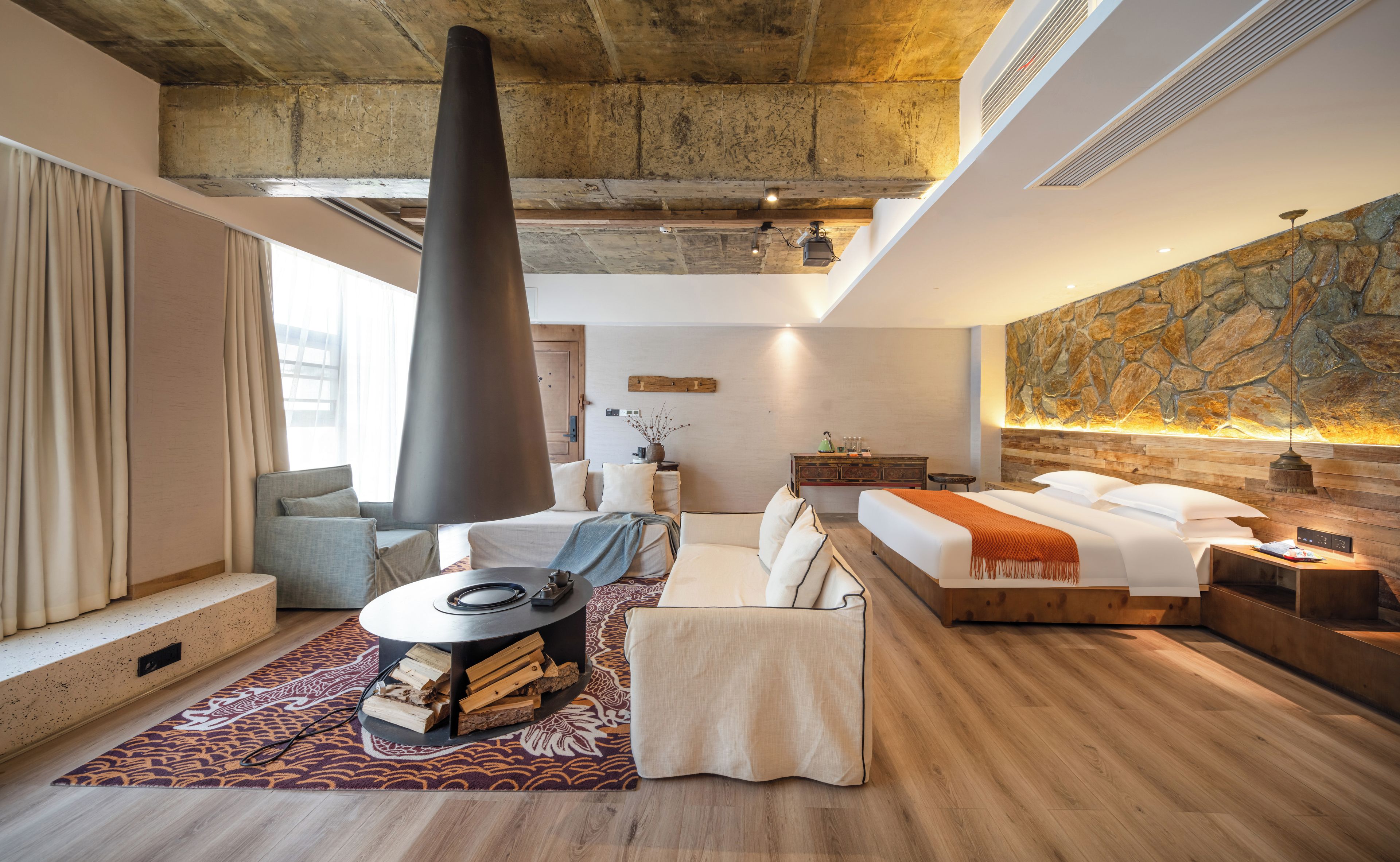 A modern hotel room with a fireplace, a bed, a sofa, and a dining table.