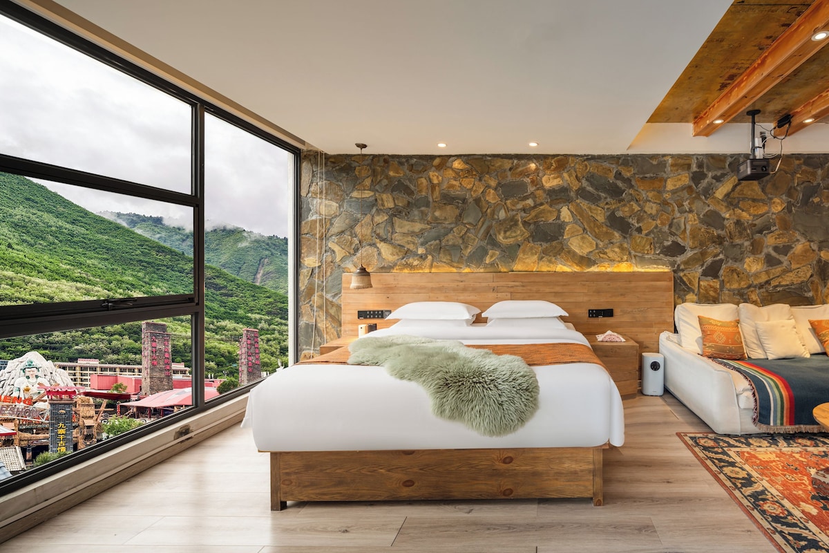 Un dormitorio moderno con una cama grande, un sofá, una mesita y una pared de piedra.