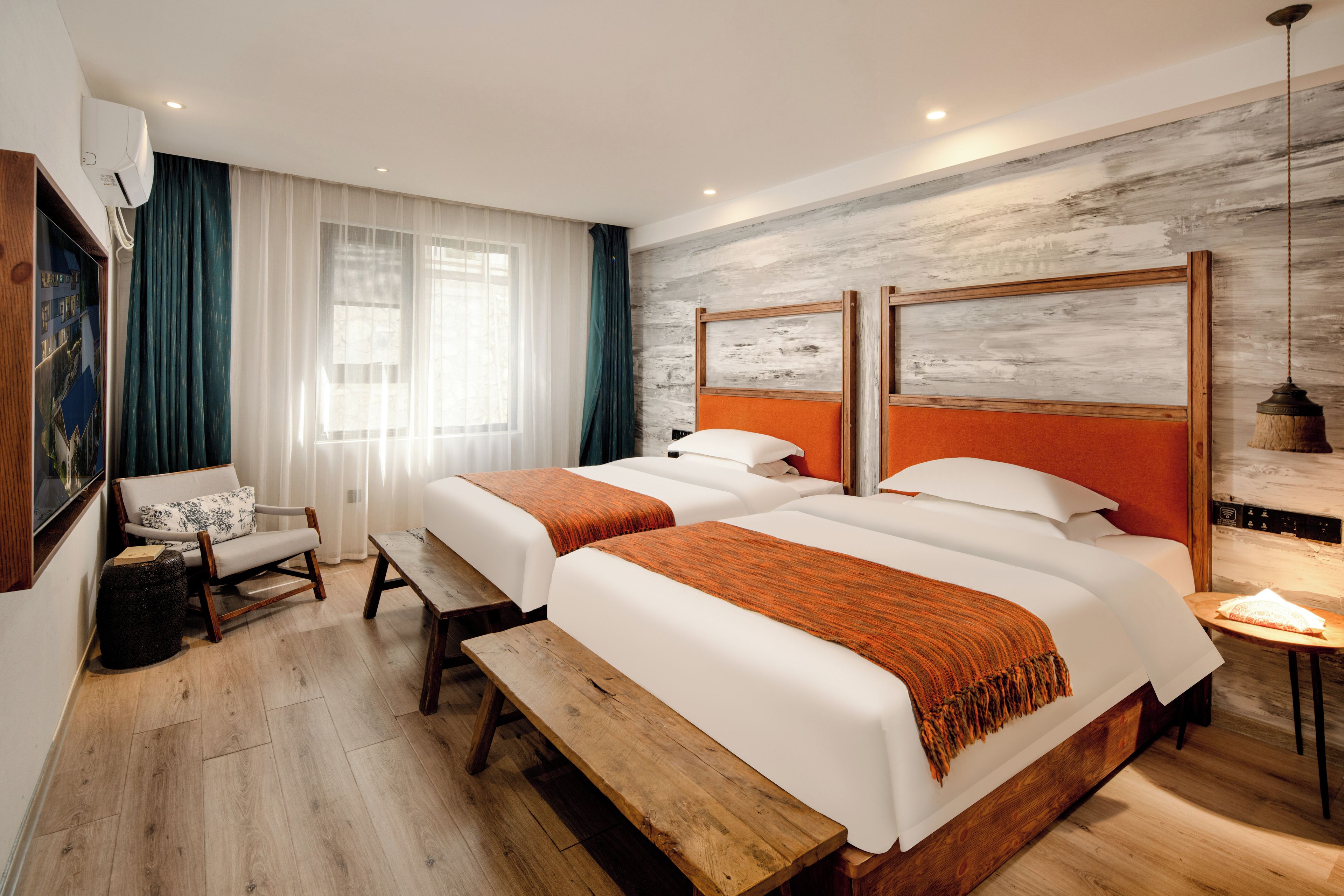 A hotel room with two beds, a bench, a chair, and a large window with curtains.