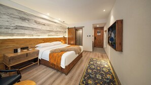 Ein modernes Hotelzimmer mit einem Holzkopfteil, einem großen Bett mit weißen Leinen, einem Nachttisch mit Lampe, einer Holzbank und einem gemusterten Teppich.