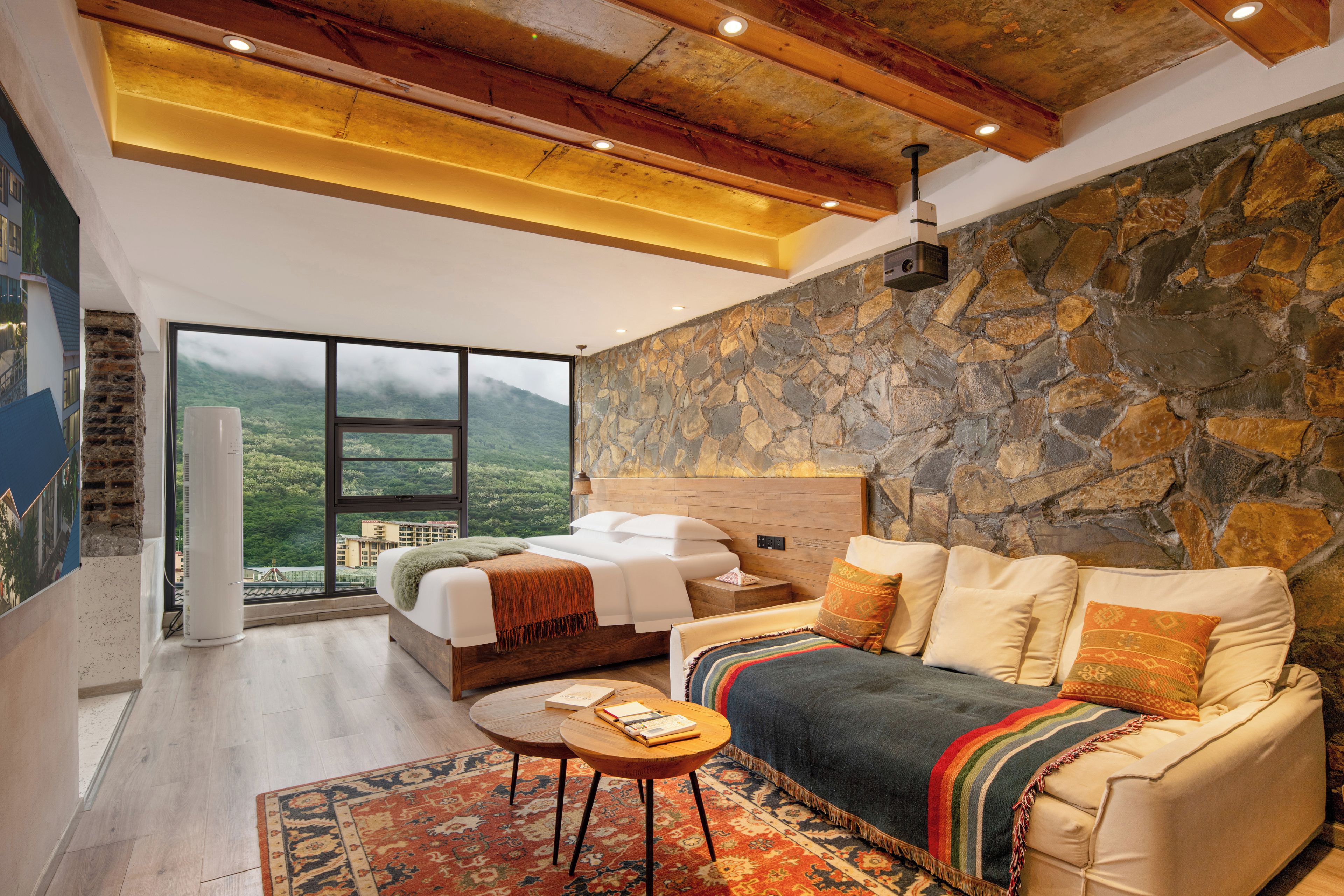 Un dormitorio moderno con pared de piedra, cama, sofá y vista a un paisaje montañoso.