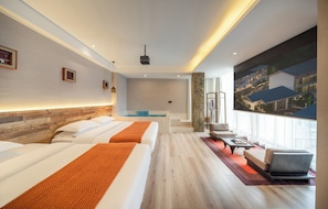 A hotel room with a large bed, a smaller bed, a seating area, a window with a view of buildings, and a pool area.