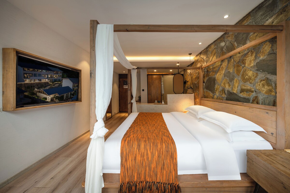 A hotel room with a large bed, a painting on the wall, and a stone wall.