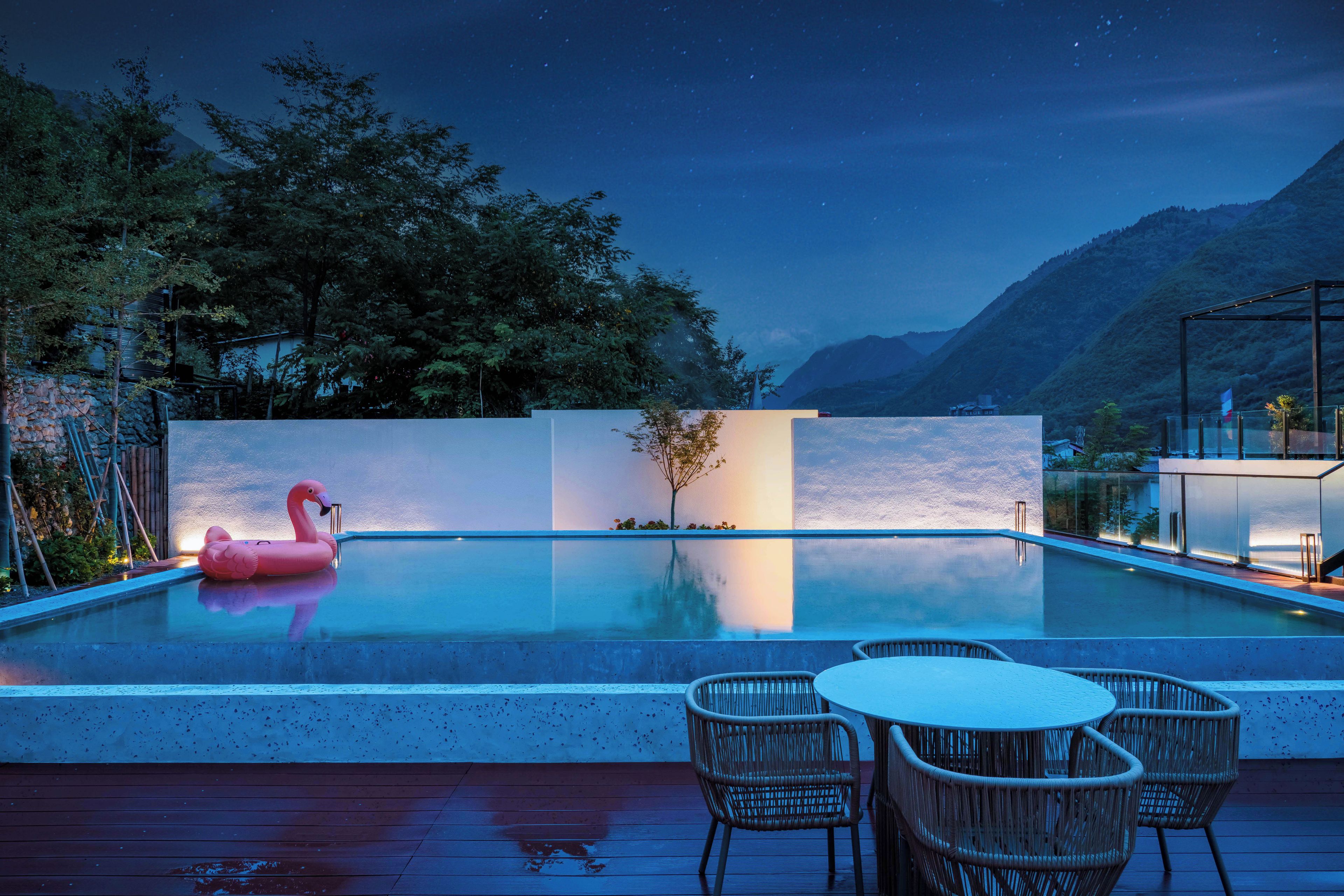 Una piscina con un flotador de flamenco, rodeada por una terraza con sillas y un cerramiento de vidrio.