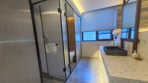 Ein modernes Badezimmer mit Duschkabine aus Glas, einer freistehenden Badewanne und einem Fenster, das für natürliches Licht sorgt.
