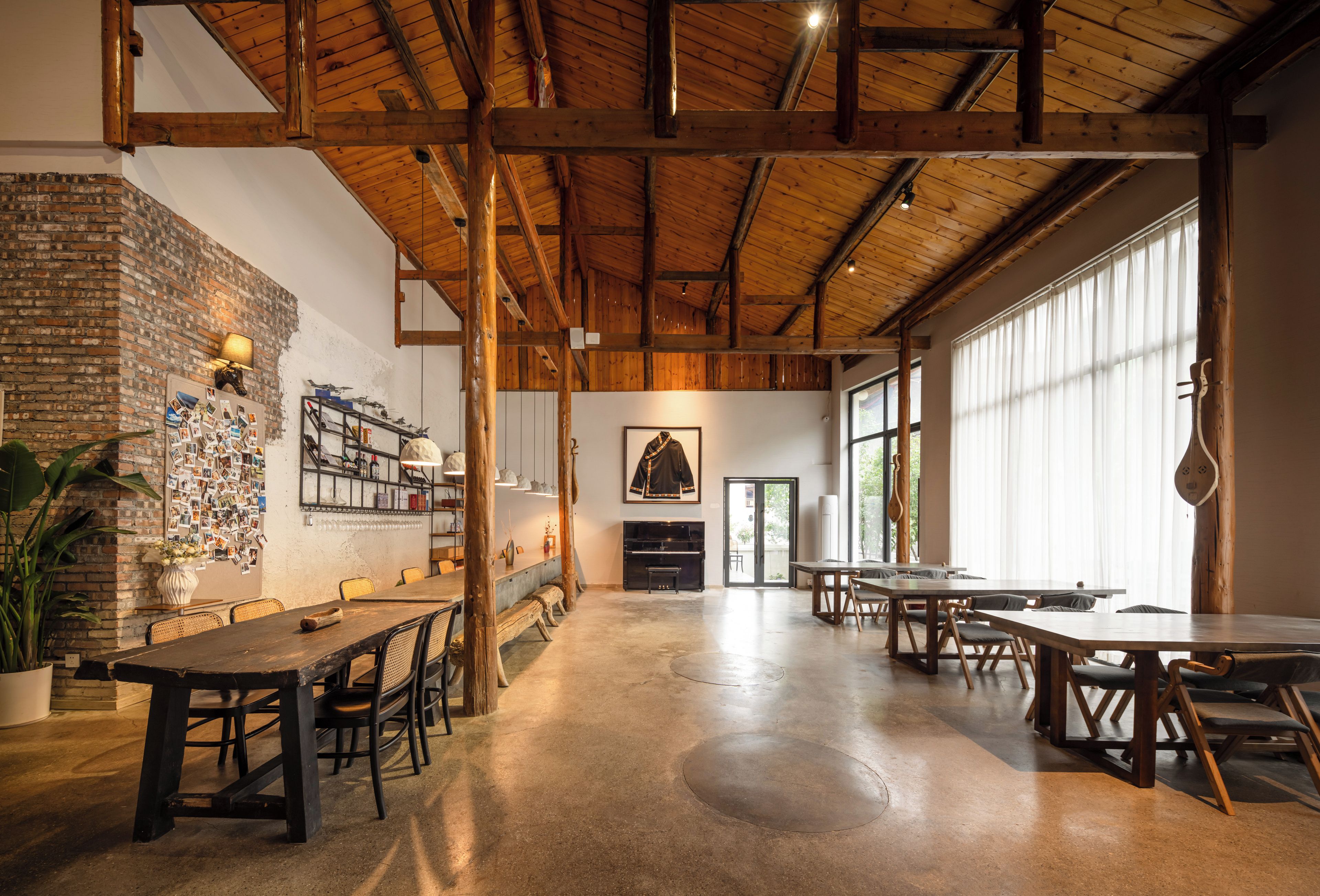 A spacious dining area with high ceilings and exposed wooden beams, featuring a brick wall with photos and a piano.