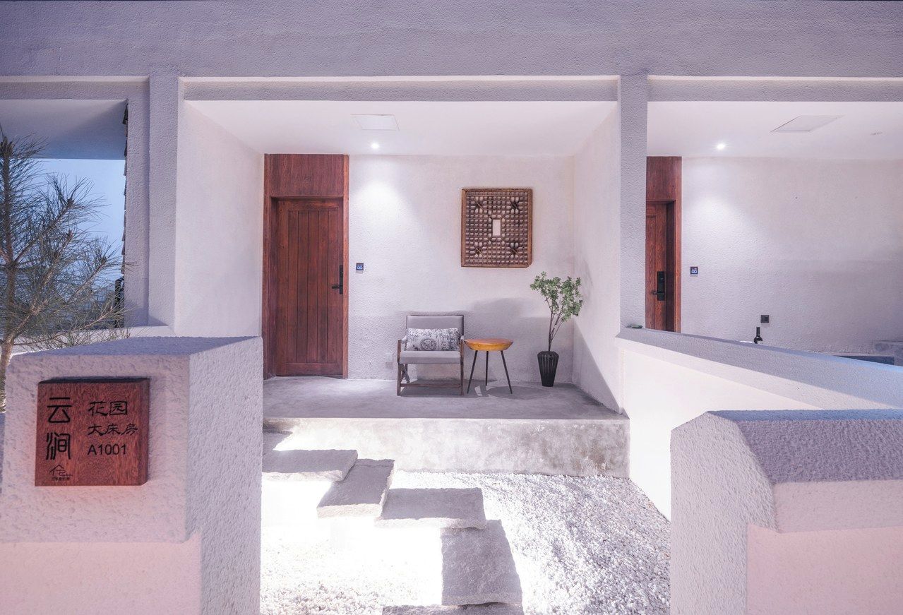 A modern hotel entrance with a wooden door, a seating area with a chair and table, and a decorative wall piece.