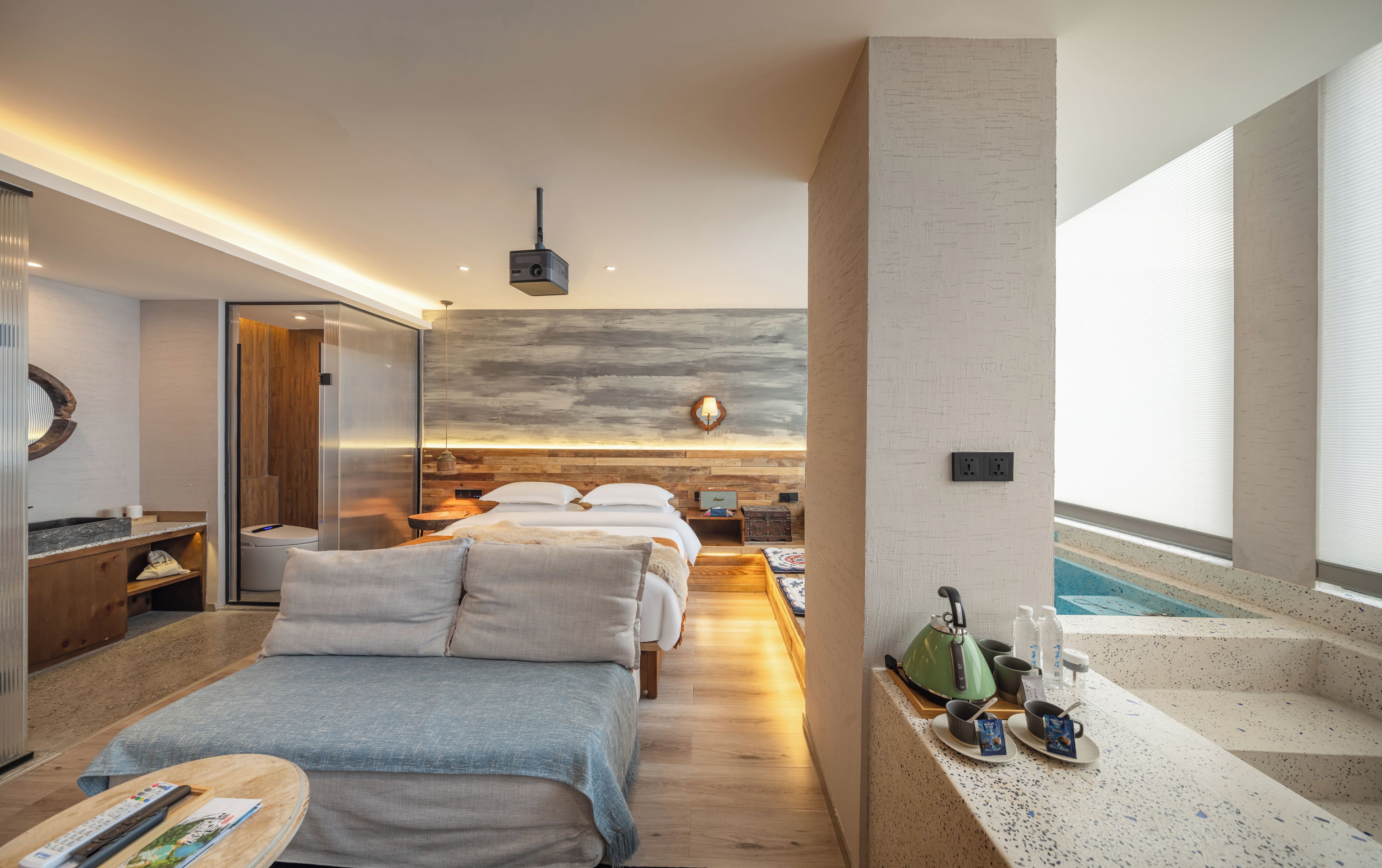 Een moderne hotelkamer met een bed, nachtkastjes, een bureau, een kleine keukenhoek en uitzicht op een zwembad.