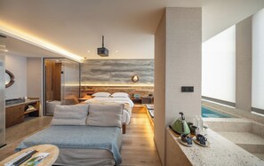 Una habitación de hotel moderna con cama, mesitas de noche, un escritorio, una pequeña cocina y vistas a una piscina.